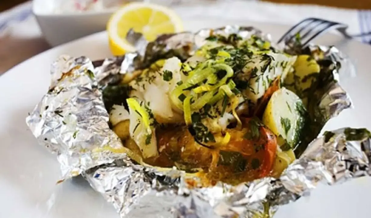 En läcker fiskpaket i ugn med potatis, tomat och örter, toppad med citron och purjolök. Enkel och smakrik middag.