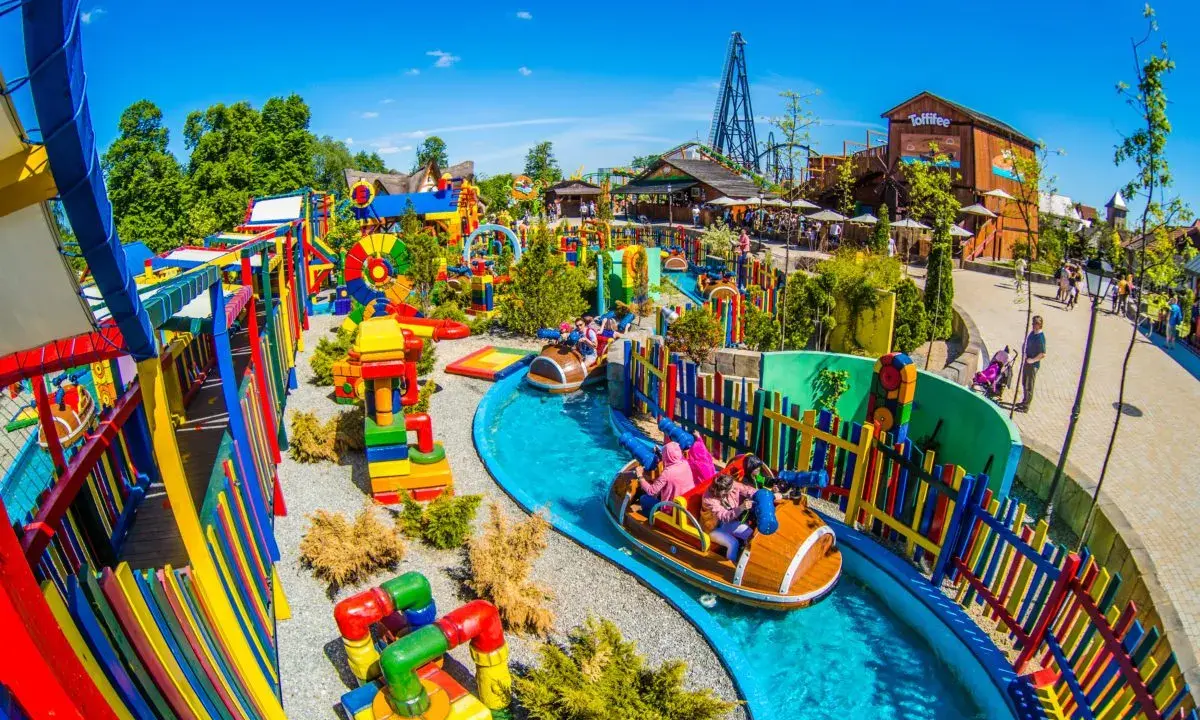 Parque acuático colorido con atracciones para niños en Cracovia. Barcas navegan por un río azul rodeado de juegos y vallas vibrantes.