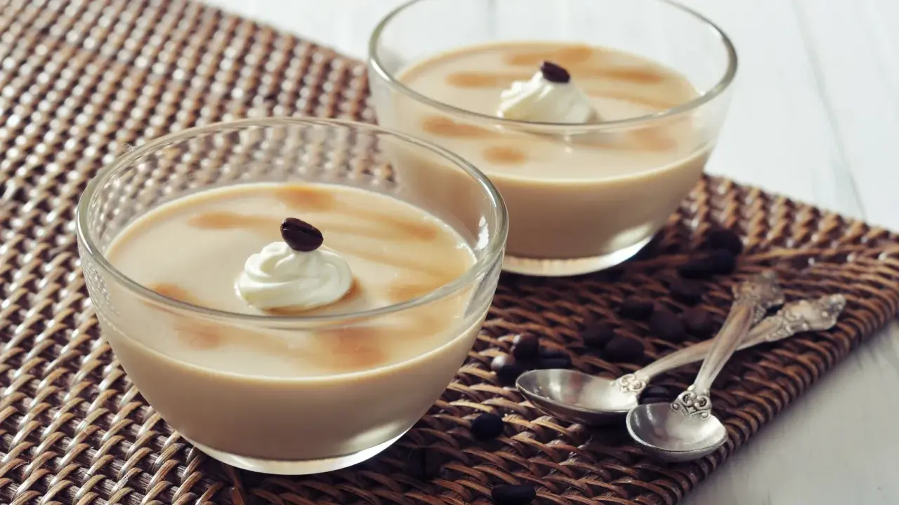 Deux coupes de **dessert au café** onctueux, garnies de crème fouettée et d'un grain de café, sur un napperon tressé.