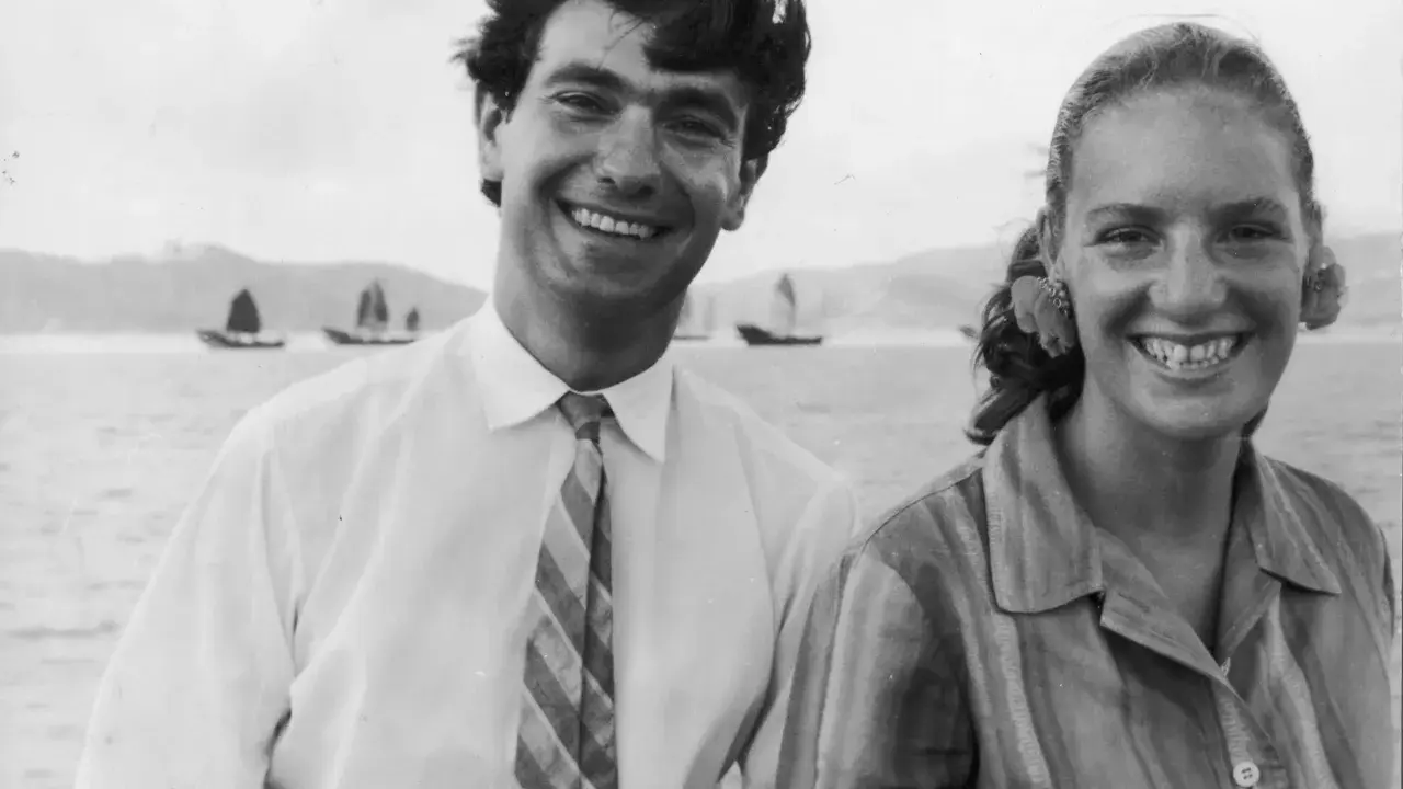 Angela Staude sorride con un uomo su una barca, con velieri sullo sfondo.