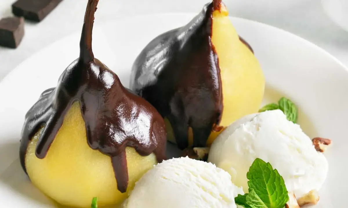 Poires pochées nappées de chocolat noir, servies avec de la glace à la vanille et des éclats de noisettes. Un délice de poire Belle Hélène.