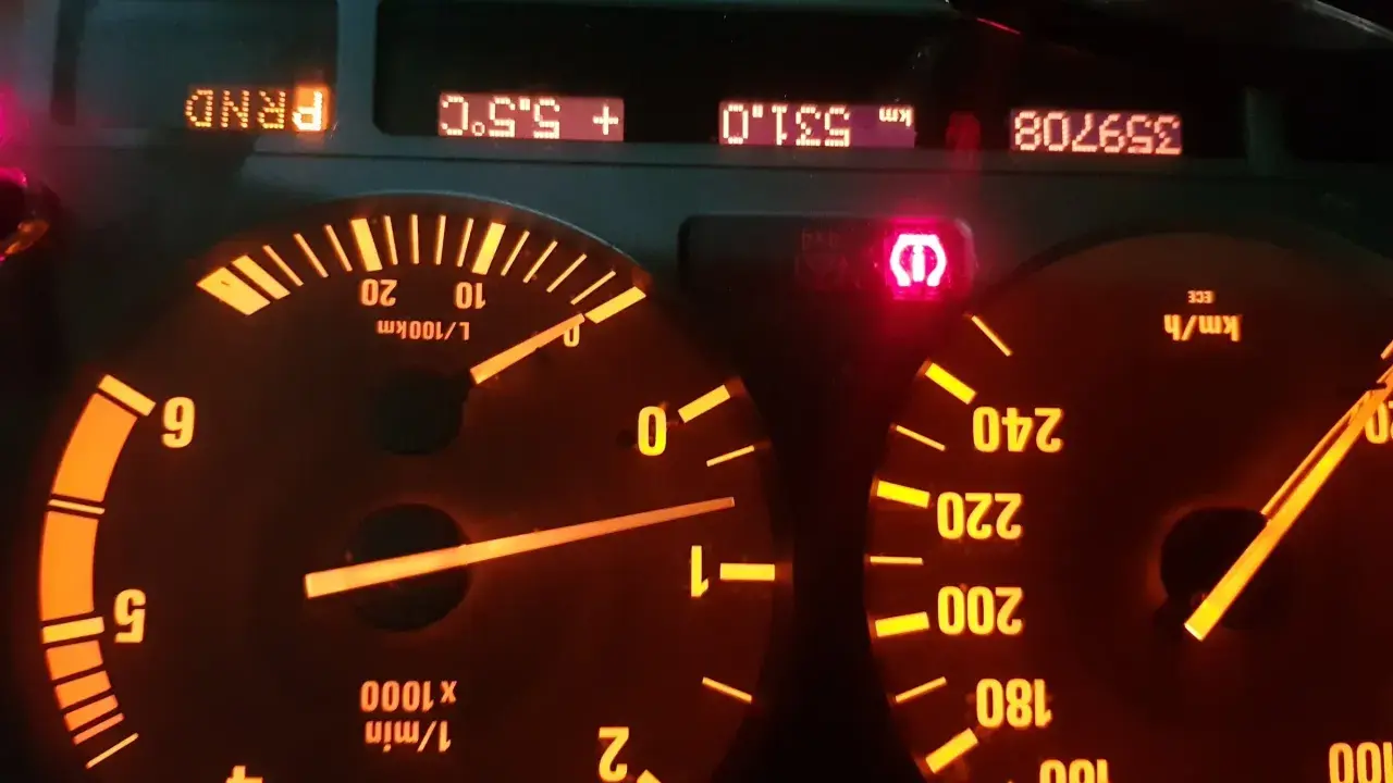 Czerwony wykrzyknik BMW świeci się na desce rozdzielczej, obok wskaźników prędkości i obrotów.