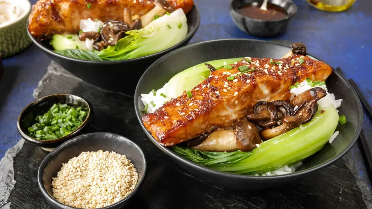 Två skålar med ris, bok choy, svamp och glaserad sous vide lax, toppad med sesamfrön och gräslök.