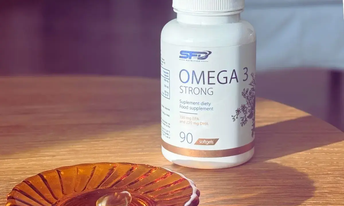 Biała butelka suplementu diety Omega 3 Strong. Na małej, bursztynowej podstawce leży jedna kapsułka. Kwasy omega 3 na co? Na zdrowie!