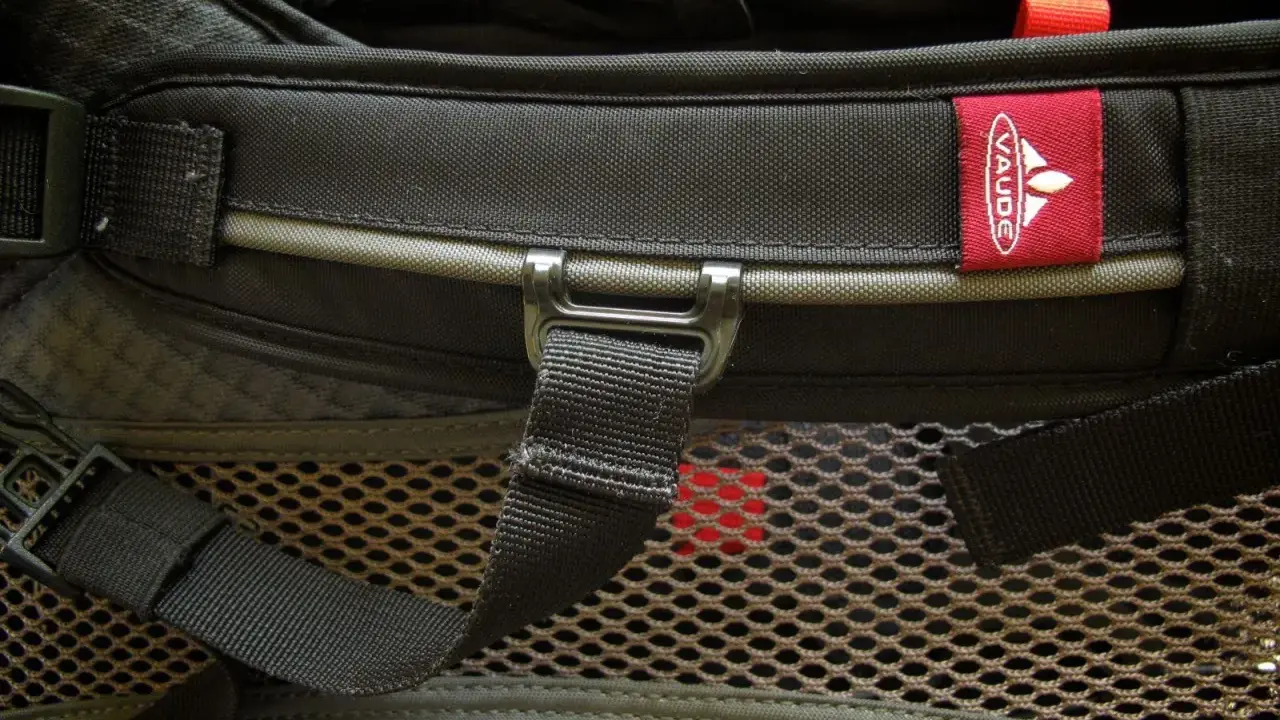 Czerwona metka z logo **Vaude** na czarnym plecaku. Firma Vaude to niemiecki producent sprzętu turystycznego.