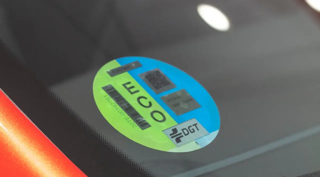 Mini etiqueta eco en parabrisas. Muestra el distintivo DGT y códigos QR para identificar vehículos de bajas emisiones.