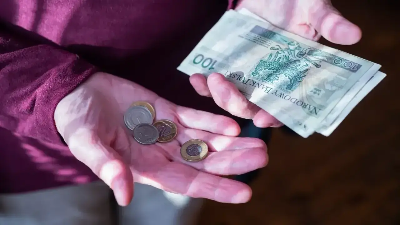 Dłonie trzymające polskie banknoty i monety. Zastanawiasz się, ile wynosi dodatek do emerytury za warunki szkodliwe?
