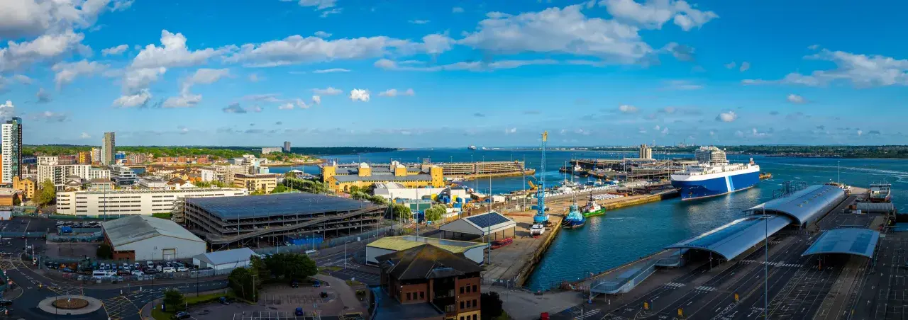 Vista panoramica del **southampton porto** con navi, gru e edifici moderni sotto un cielo azzurro con nuvole bianche.