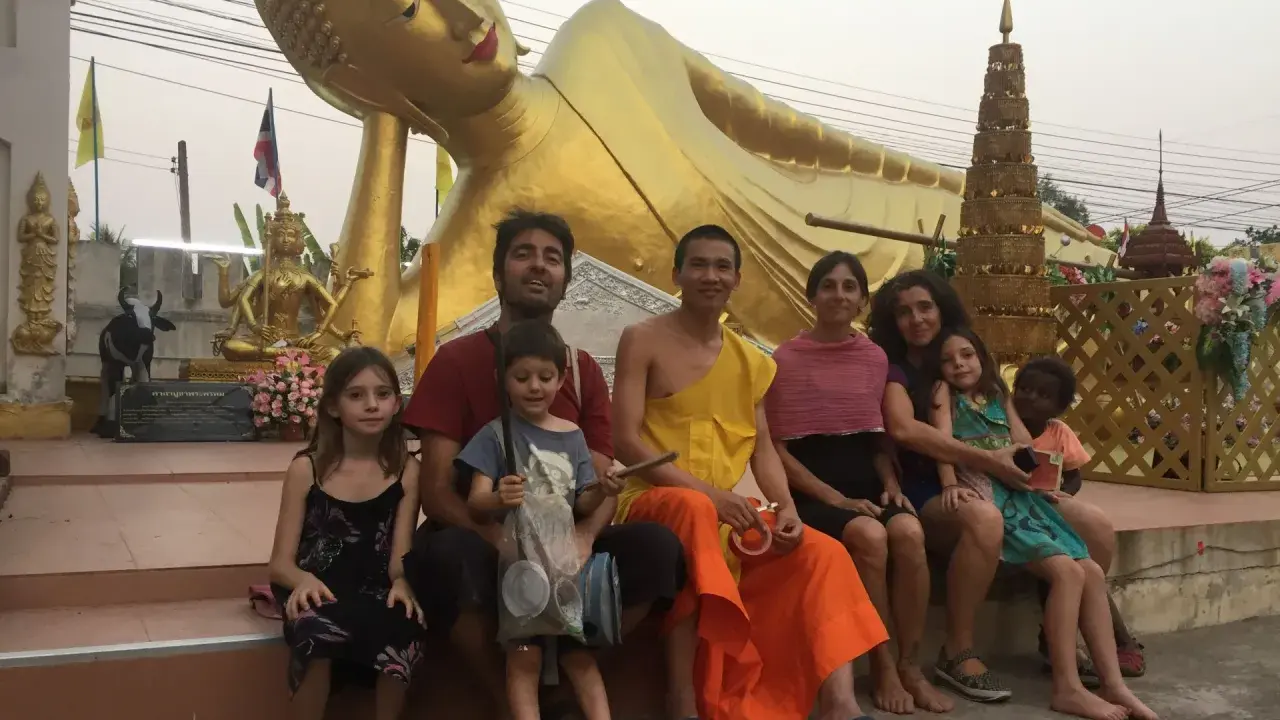 Familia disfrutando de un viaje a Asia con niños, sentados frente a una estatua dorada de Buda reclinado.