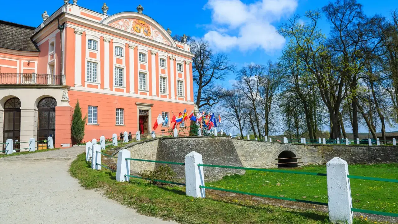 Pałac w Kurozwękach, z flagami narodowymi przed wejściem, zaprasza do odkrywania jego atrakcji.