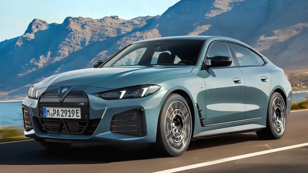 Der neue BMW i4 Facelift in einem eleganten Blau fährt auf einer Küstenstraße vor einer Bergkulisse.