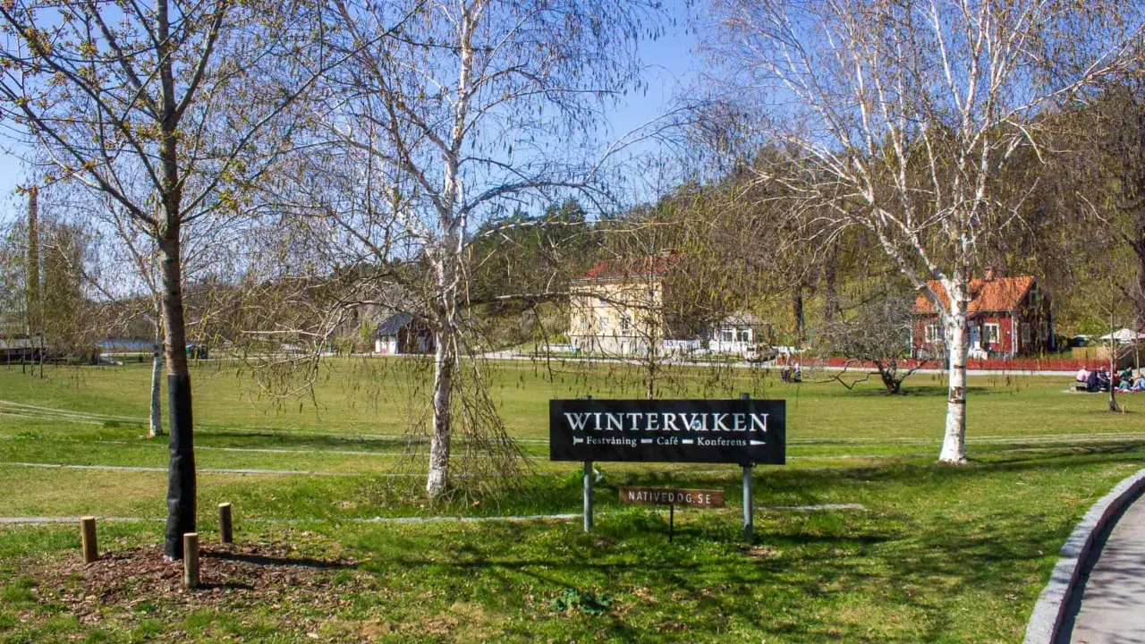 Vinterviken Stockholm, en grönskande park med träd och byggnader. En skylt visar "Winterviken - Festvåning - Café - Konferens".