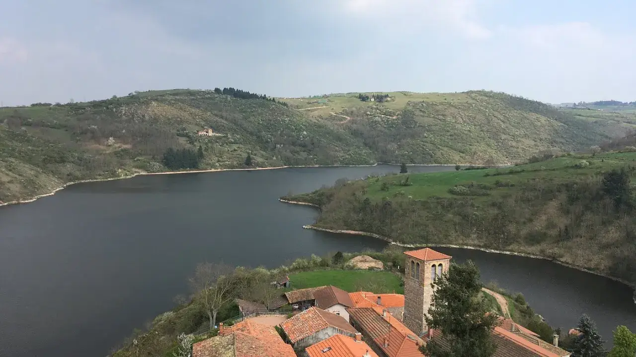 Villaggio pittoresco con tetti rossi e campanile affacciato su un lago serpeggiante, incastonato tra colline verdi vicino a Roanne, Francia.