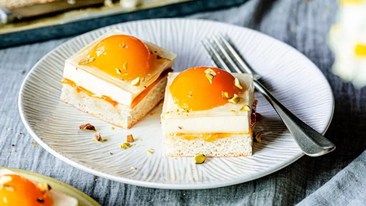 Zwei exquisite Stücke spiegeleikuchen mit pudding, garniert mit Pfirsich und Pistazien, auf einem Teller mit einer Gabel.