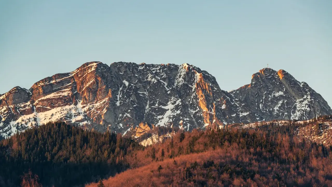 Skały Giewontu, ośnieżone i oświetlone słońcem, wznoszą się nad lasem. Choć trudno określić jaką wysokość ma Giewont, jego majestat robi wrażenie.
