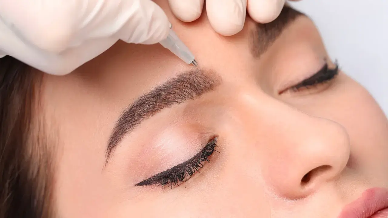Main d'une esthéticienne réalisant des sourcils permanent effet naturel sur une cliente.