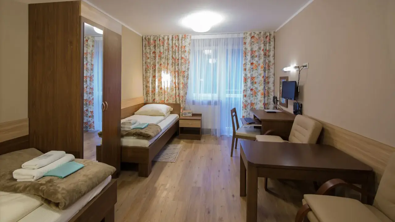 Pokój w sanatorium Włókniarz Busko-Zdrój: dwa łóżka, szafa, biurko z komputerem i stolik.