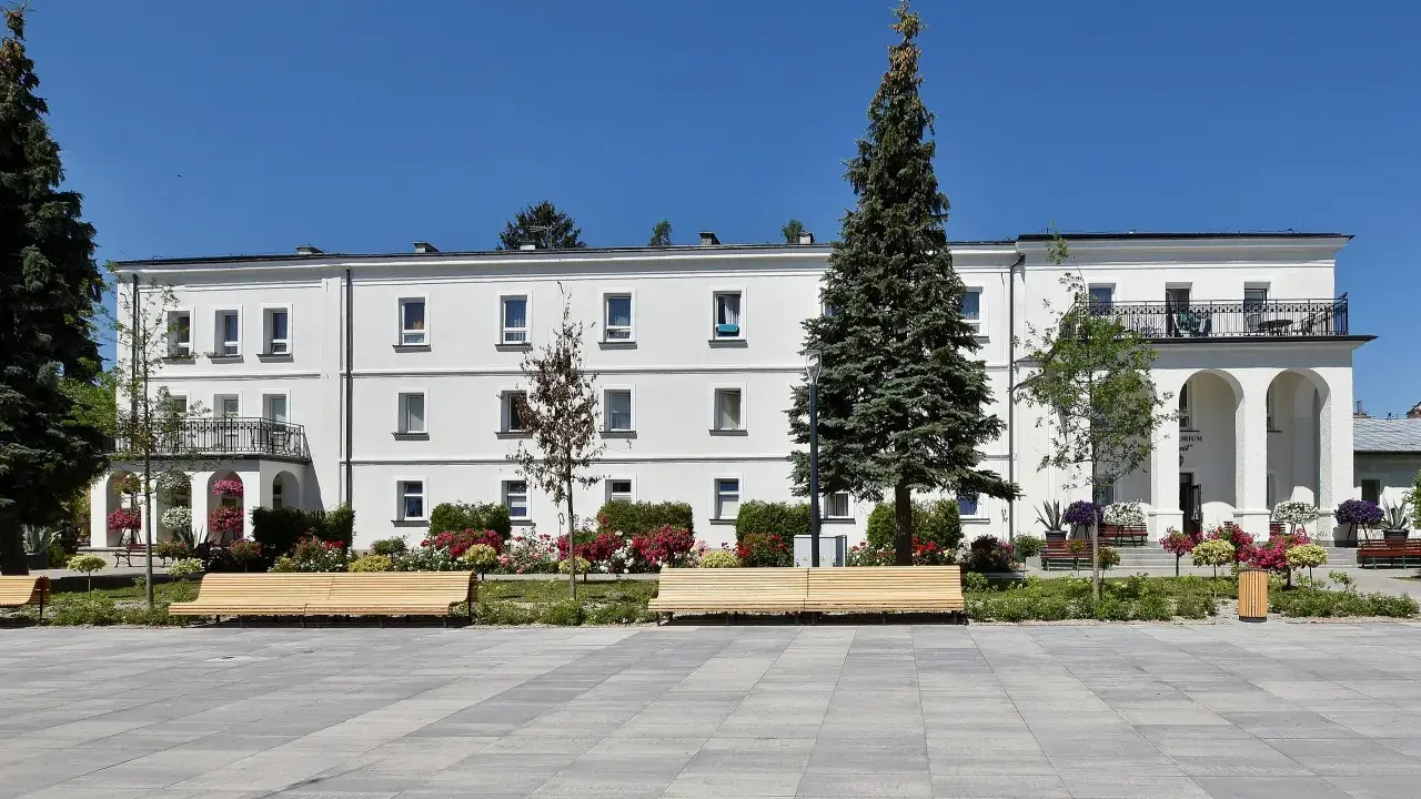 Sanatorium Świt w Solcu-Zdroju, biały budynek z balkonami i łukami, otoczony zielenią i kwiatami.