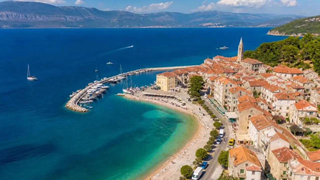 Malownicze miasteczko na wyspie Brač z portem pełnym łodzi, plażą i kamiennymi domami pod czerwonymi dachami.