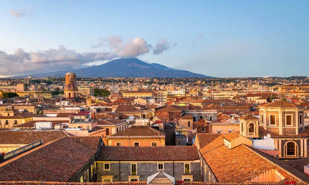 Vista panoramica di Catania con l'Etna sullo sfondo. Tetti rossi, cupole e palazzi storici offrono spunti per le cose da fare a Catania.