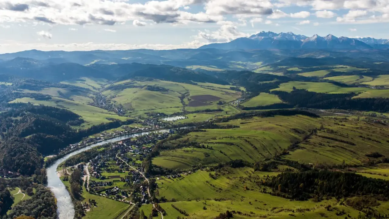 Widok na dolinę z rzeką i miasteczkiem, w oddali majaczą góry Tatry, które przypominają trzy korony. Wysokość widoku zapiera dech.