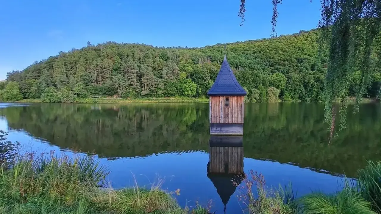 Holzhaus mit spitzem Dach, wie eine kleine Kirche im See, spiegelt sich im ruhigen Wasser.
