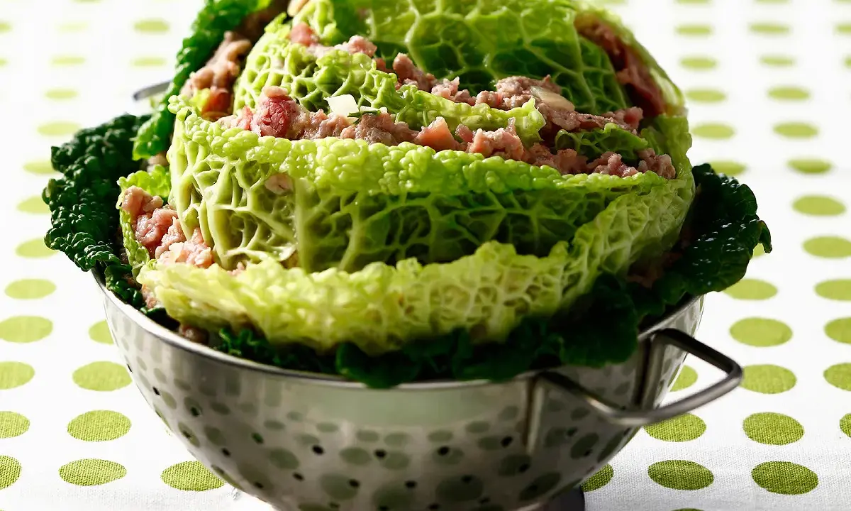 Un chou farci, recette traditionnelle, présenté dans une passoire en métal. Les feuilles de chou vert vif enrobent une garniture de viande hachée.