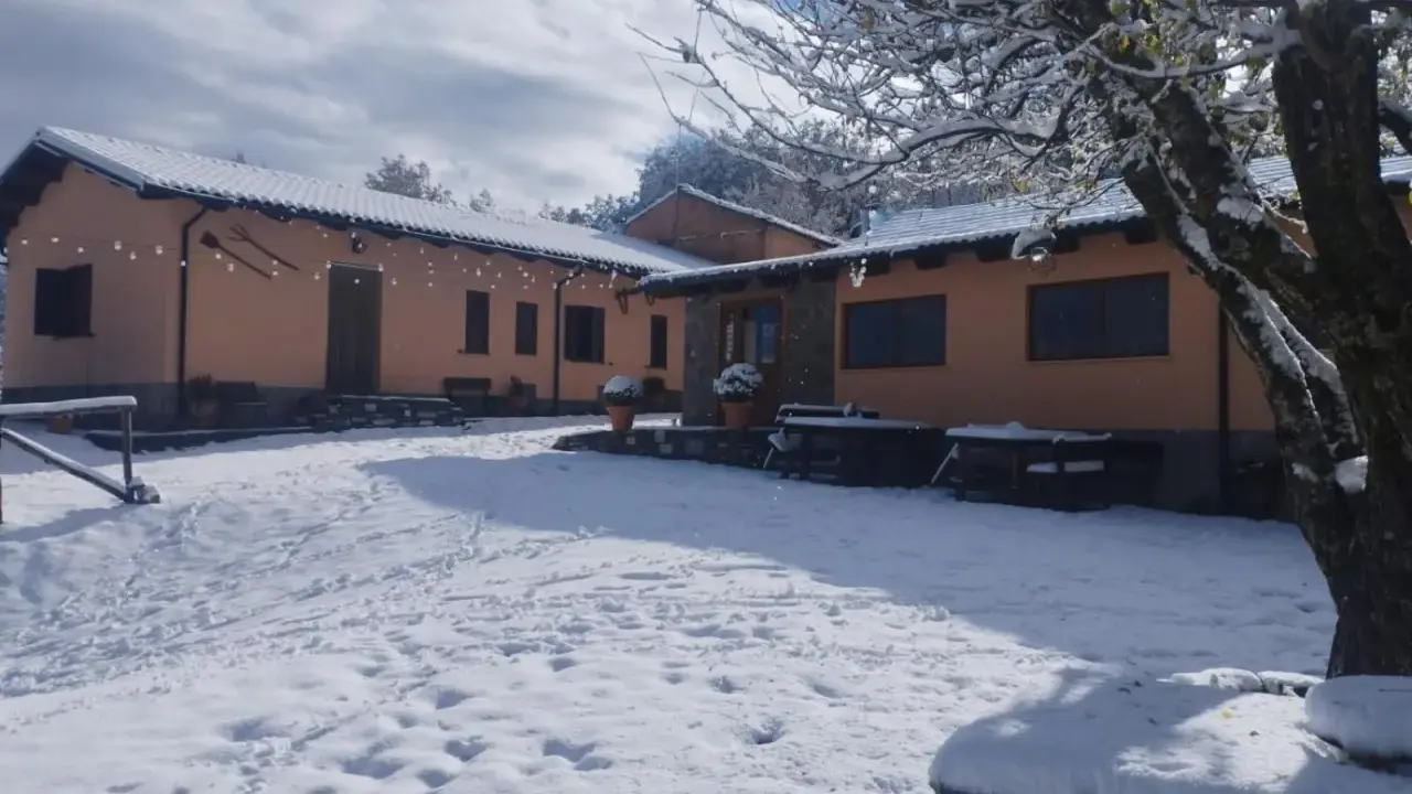 Agriturismo Acqua Bianca imbiancato dalla neve. Un paesaggio invernale incantevole con edifici color pesca e un cielo azzurro con nuvole bianche.
