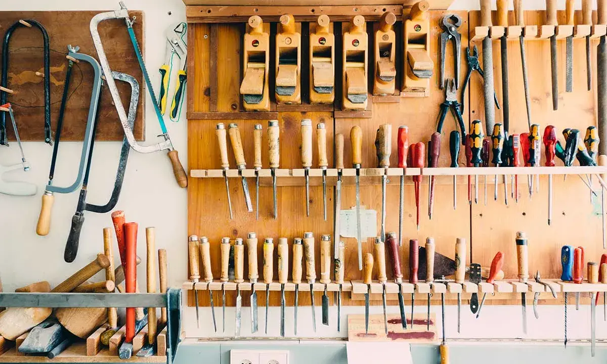 Un bel aménagement atelier avec des rabots, des scies, des tournevis et d'autres outils de menuiserie bien rangés sur un panneau en bois.