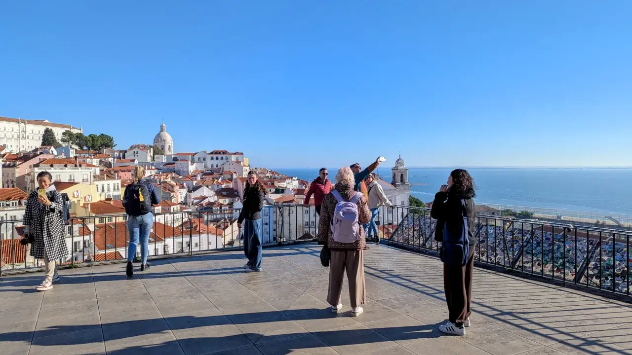 Blick vom Miradouro Portas do Sol auf Lissabons Dächer und das Meer. Touristen genießen die Aussicht.