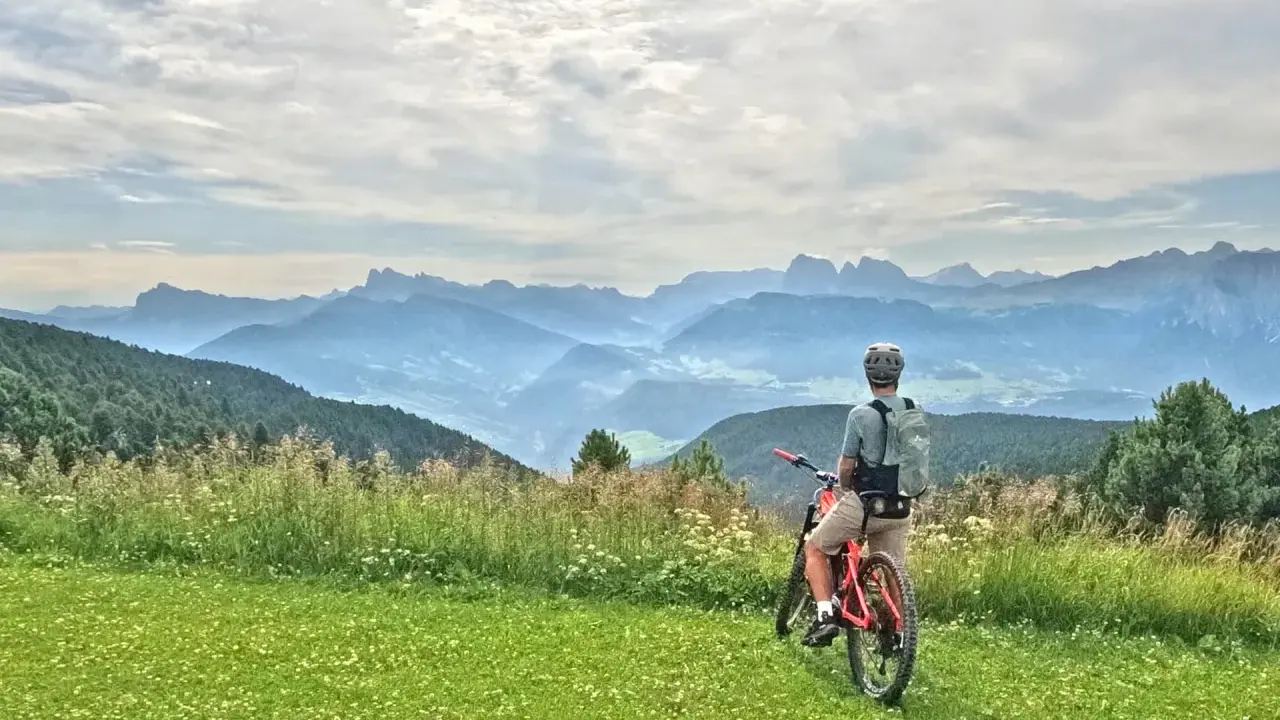 Ciclista con bici da enduro ammira il panorama montano. Un'avventura in bici, forse a Cervia, tra prati fioriti e cime nebbiose.