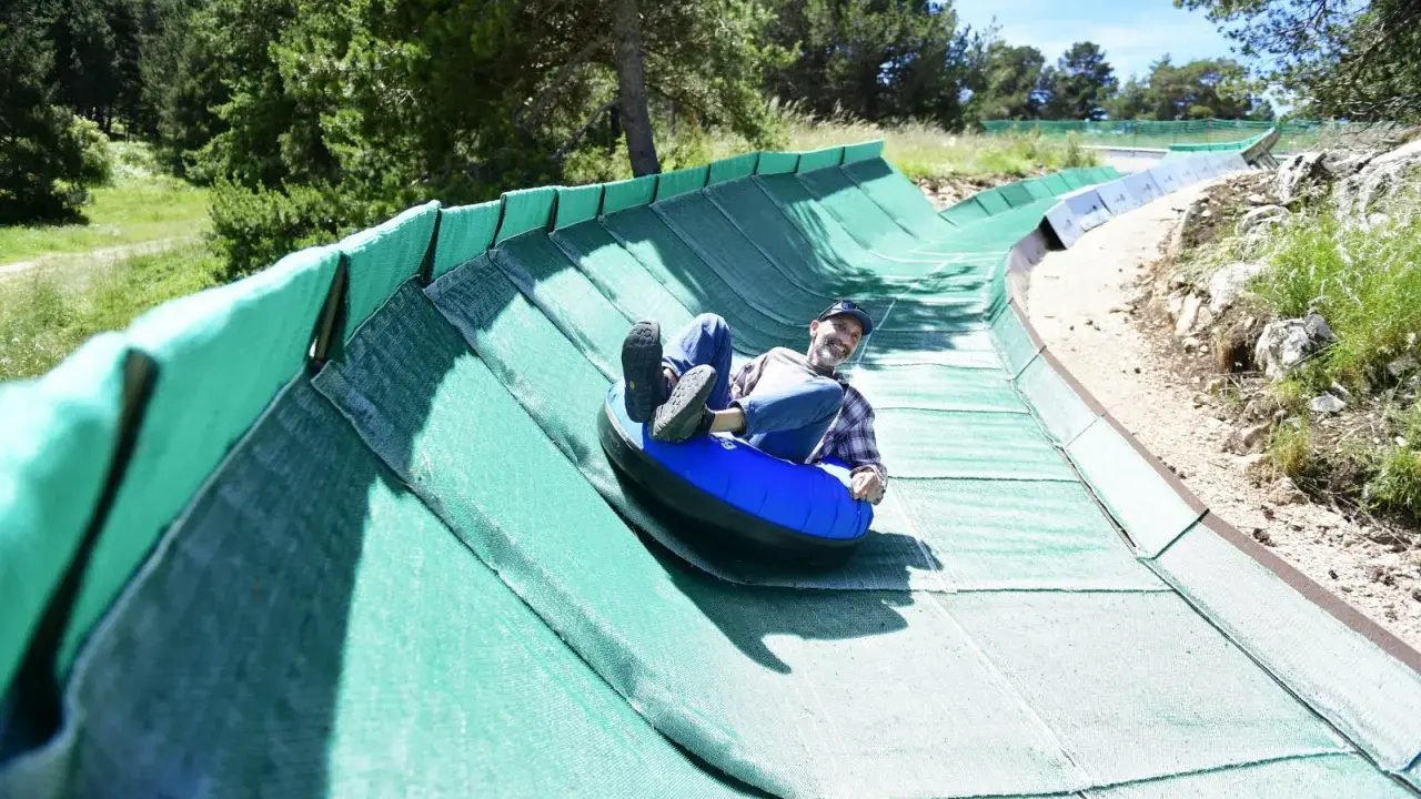 Un homme souriant dévale une piste verte en luge gonflable, profitant des activités Mont Ventoux.