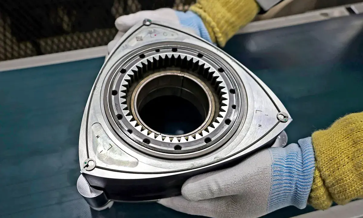 Rotor silnika Wankla, kluczowy element innowacyjnych samochodów z silnikiem Wankla, trzymany w rękawiczkach.