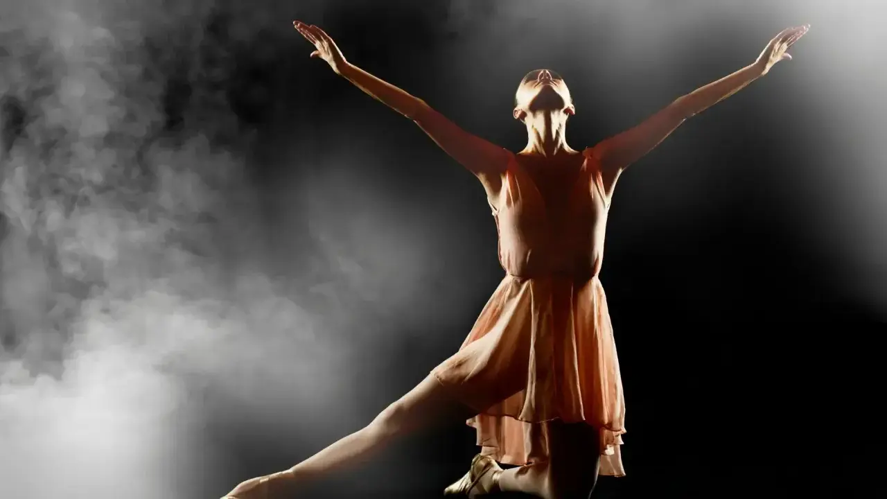 En ballerina i en ljusrosa klänning utför en graciös rörelse i klassisk balett, omgiven av dramatisk rök och ljus.