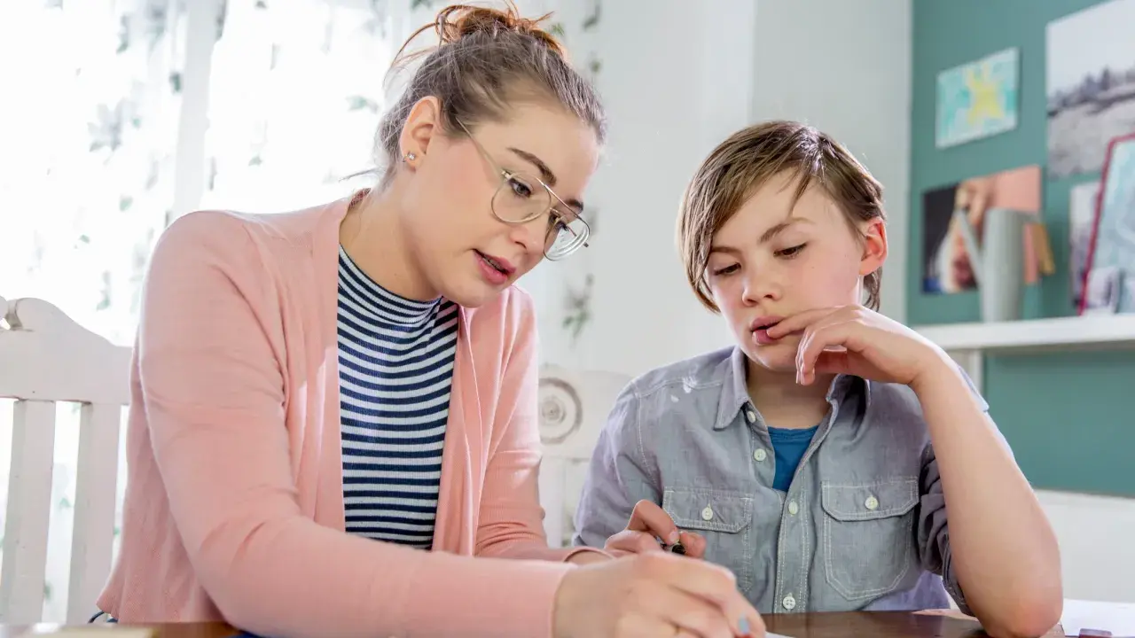 Junge Frau bietet Nachhilfe an. Sie erklärt einem Jungen konzentriert eine Aufgabe auf Papier.