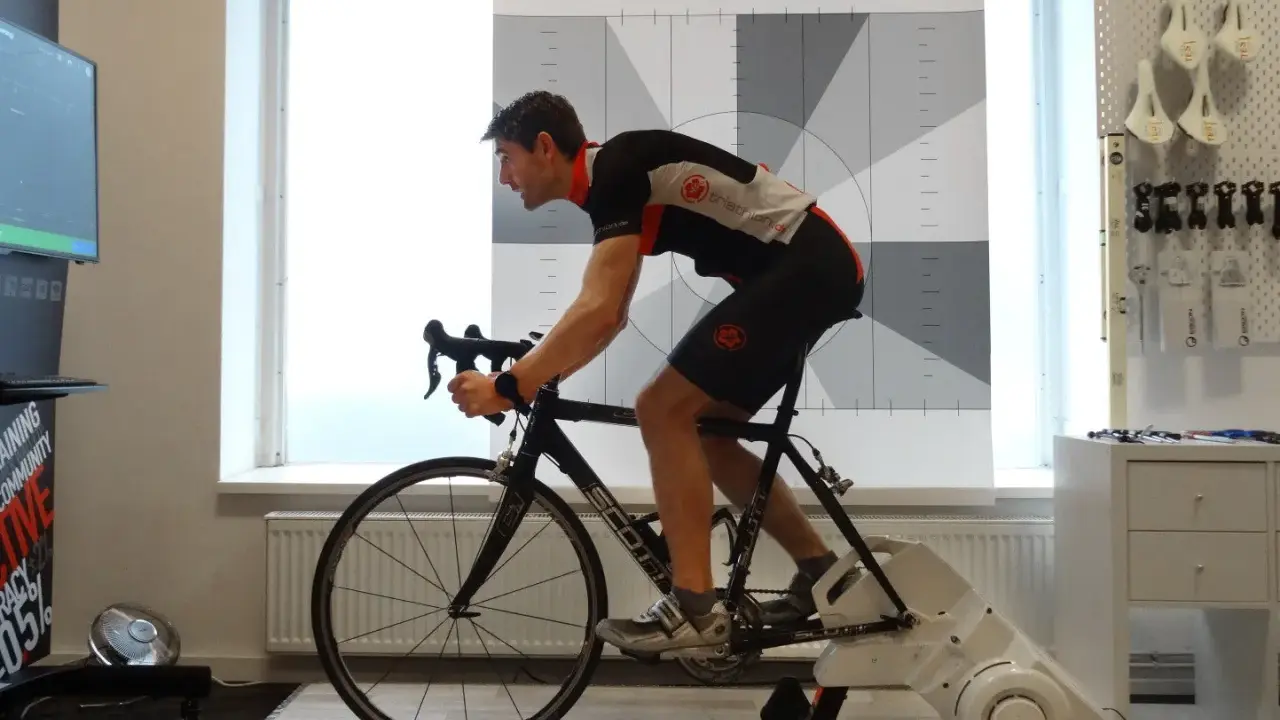 Mann auf einem Rennrad-Trainer, der sein Lungenvolumen trainiert. Hinter ihm eine Wand mit Triathlon-Logo und Messmarkierungen.