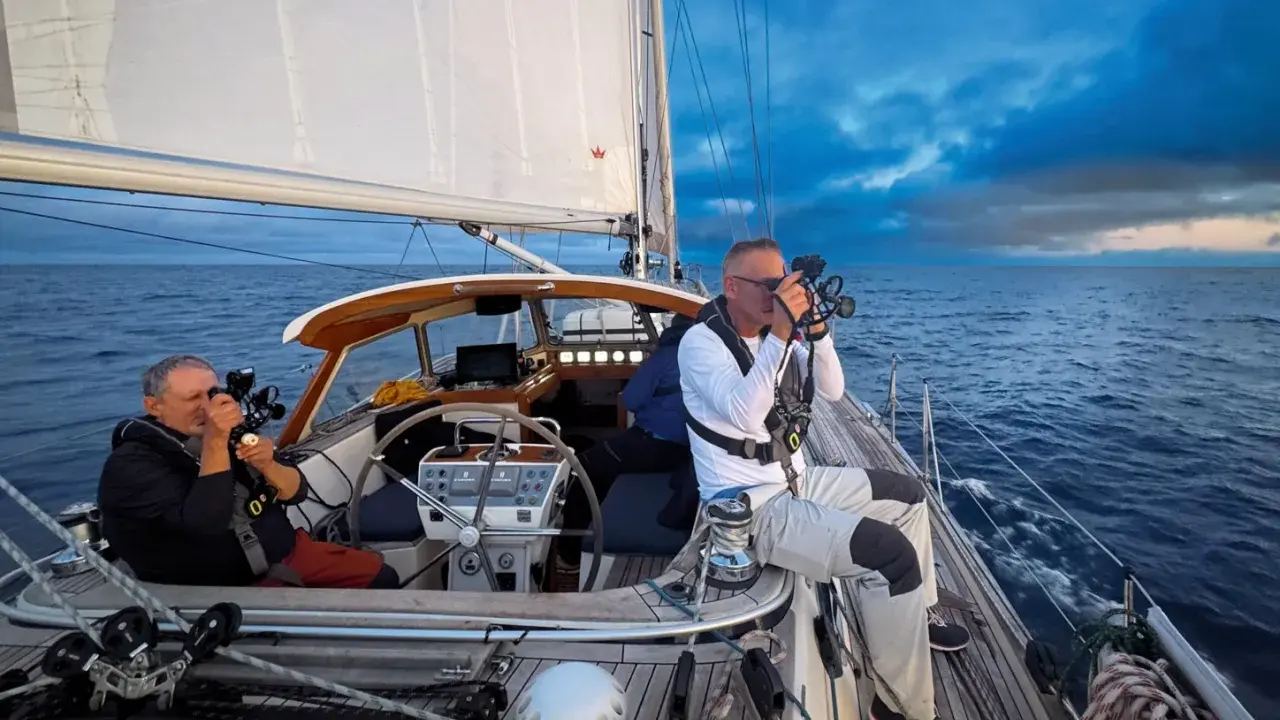 Leon Schulz und ein Kollege filmen auf See. Die Segel sind gesetzt, die Wellen schlagen gegen das Boot.