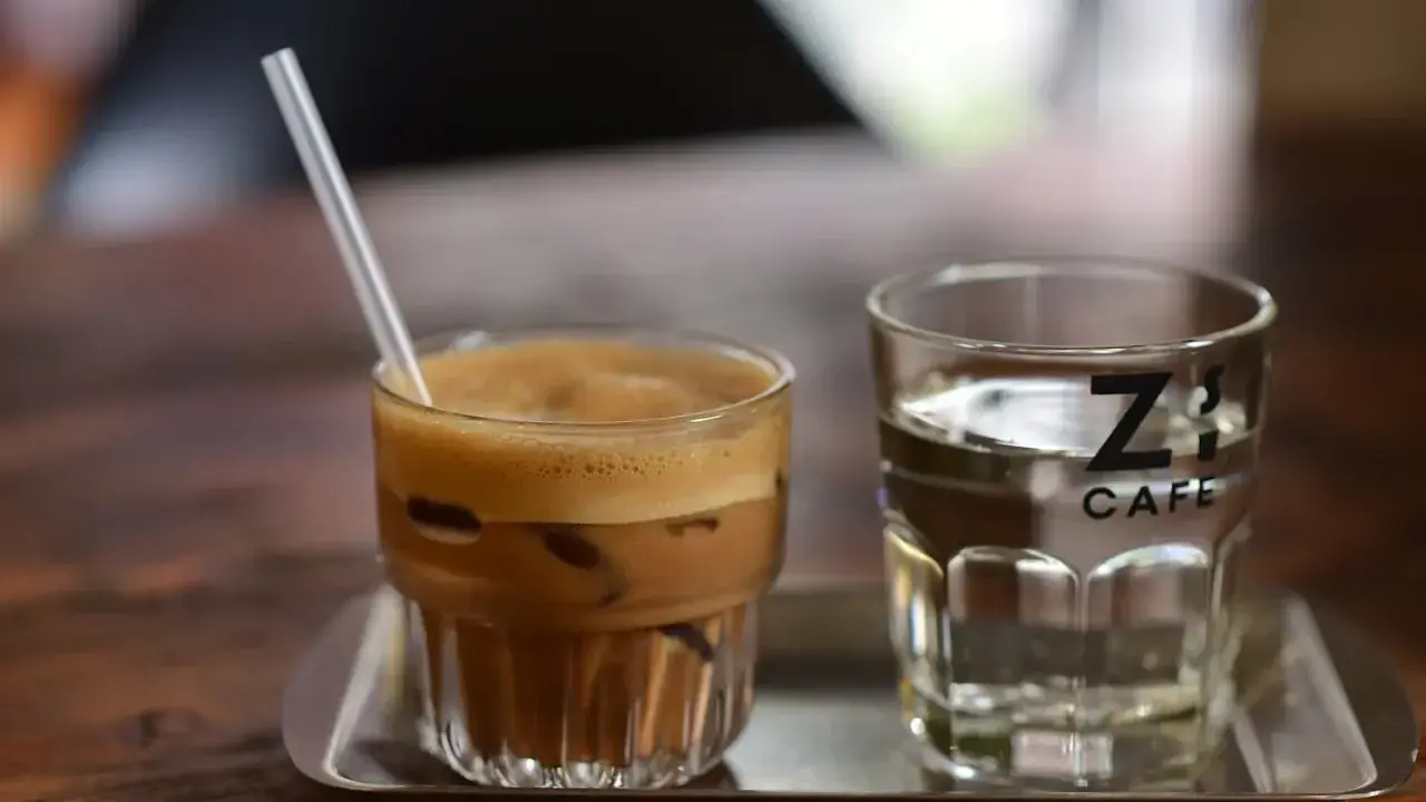Kawa z lodem i słomką obok szklanki wody. Czy kawa jest moczopędna? Z's Cafe.