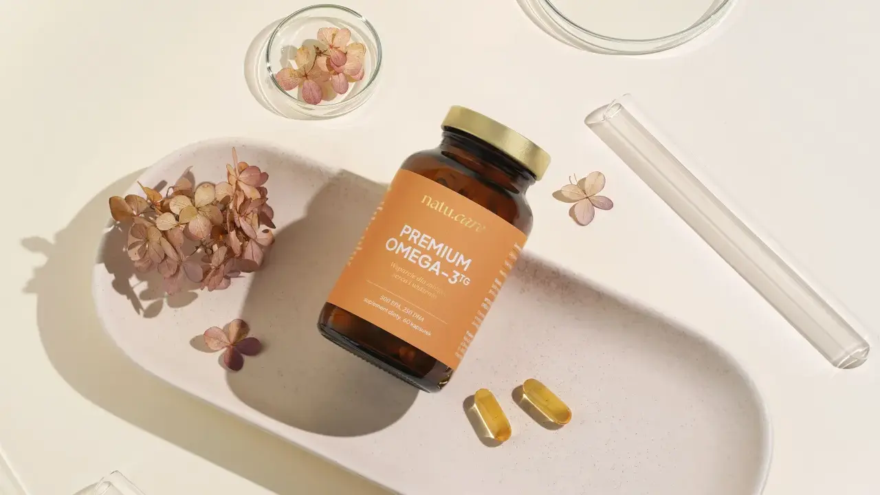 Butelka z suplementem omega 3 dla niemowląt, dwie kapsułki i suszone kwiaty na ceramicznej tacce.