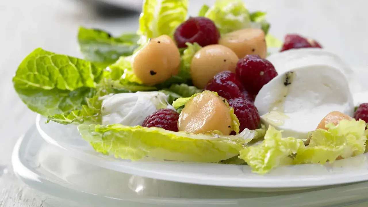Erfrischender melonensalat mit mozzarella, Himbeeren und knackigem Salat. Ein leichter Genuss für warme Tage.