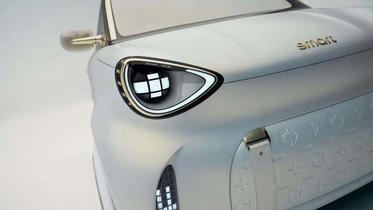 Dettaglio di un'auto elettrica Smart, con un faro futuristico e il logo dorato. Nuovi modelli in arrivo.