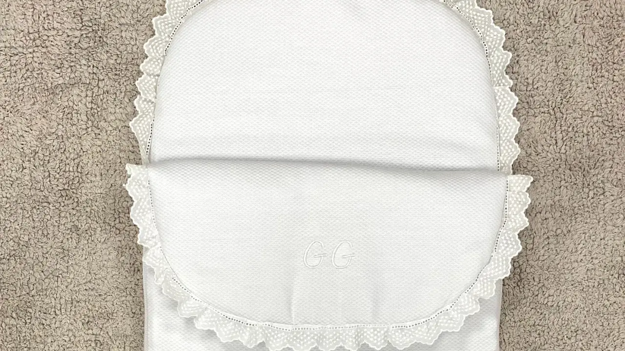 Patrón saco bebé capazo blanco con encaje y iniciales GG bordadas. Perfecto para un dulce descanso.
