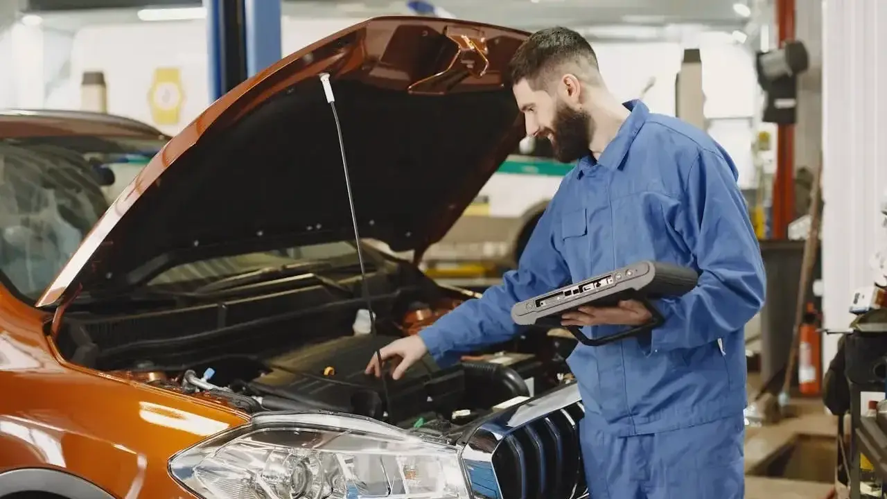 Mechanik z komputerem diagnostycznym sprawdza silnik. Zastanawiasz się, ile trwa wymiana oleju? To szybka usługa.