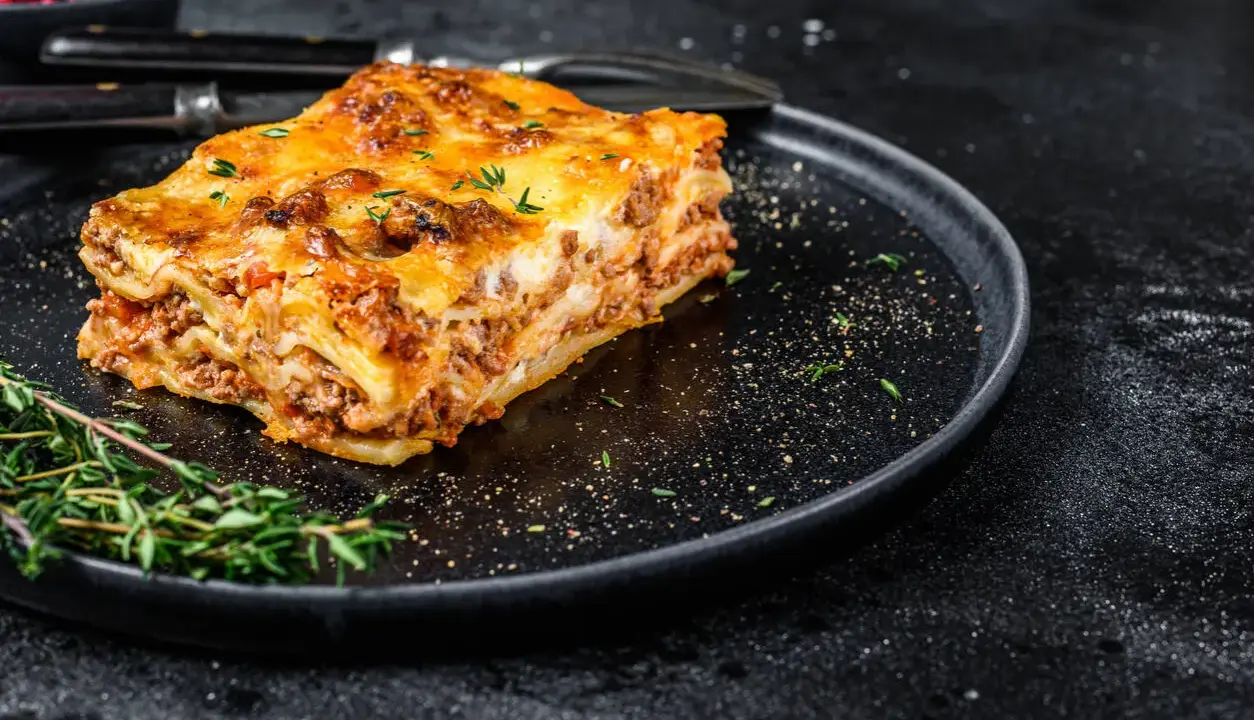 En bit gyllene lasagne på en svart tallrik, perfekt comfort food med köttfärs och ost.