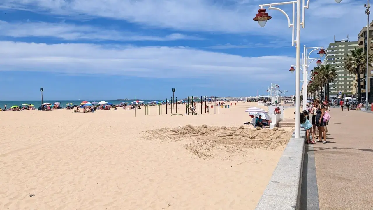Sonniger Tag am Playa Victoria in Cádiz. Menschen entspannen sich unter bunten Sonnenschirmen, während Kinder am Strand spielen.
