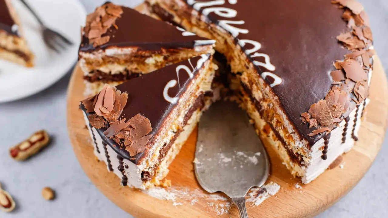 Pyszny tort snickers bez pieczenia, udekorowany czekoladą i wiórkami. Idealny na deser!