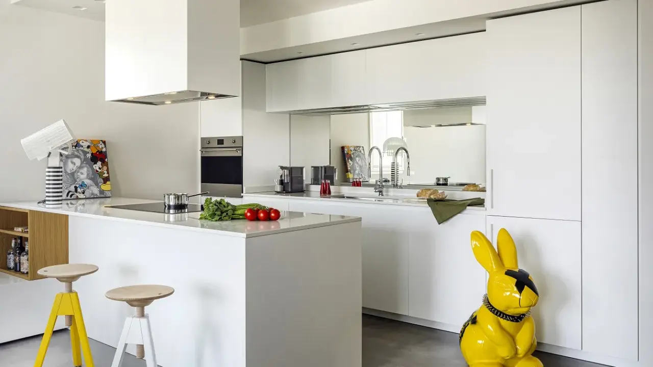 Cucina moderna con isola centrale e sgabelli. La differenza tra RAL 9003 e 9010 è sottile, ma qui il bianco puro domina, con un tocco di giallo dato da un coniglio decorativo.