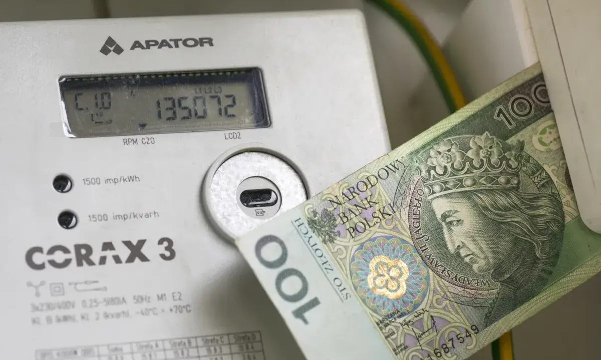 Licznik energii elektrycznej z banknotem 100 zł. Wysokie rachunki za prąd to problem, ale dodatek energetyczny może pomóc.