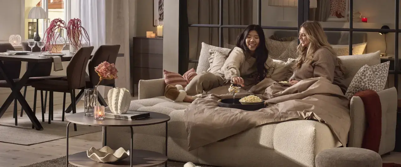 Två vänner myser i en stor sov fåtölj med popcorn och filtar.