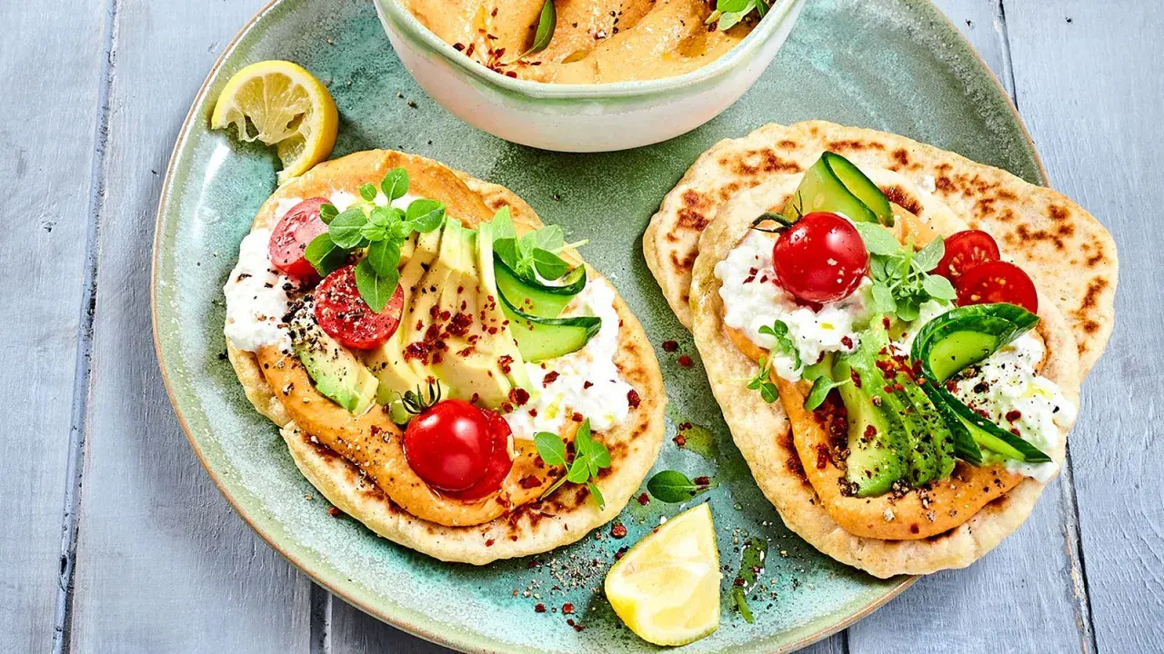 Leckere kalte gerichte ohne kochen: Fladenbrot mit Hummus, Avocado, Tomaten, Gurke und Frischkäse. Garniert mit Kräutern und Zitrone.